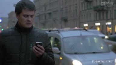 年轻的男子在一个寒冷的雨天在城市使用智能手机，他站在路边与紧张